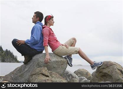 Couple sitting back to back on rocks by ocean
