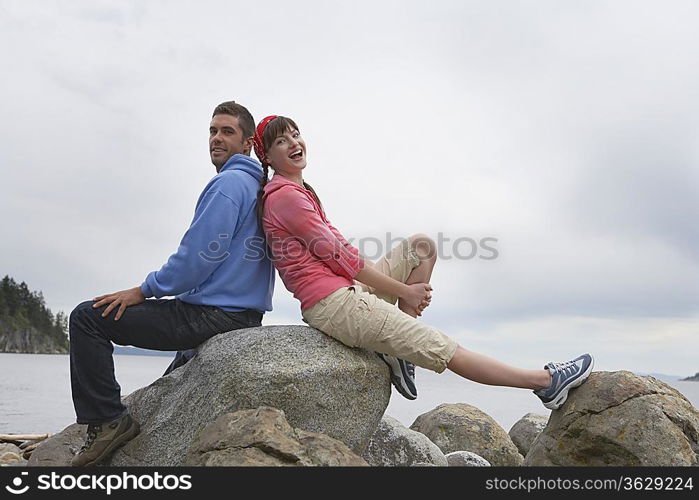 Couple sitting back to back on rocks by ocean, portrait