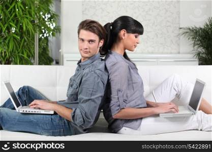 Couple sitting back to back while using their laptops
