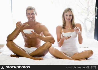 Couple sitting in bed eating cereal and smiling