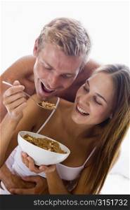 Couple sitting in bedroom eating cereal and smiling