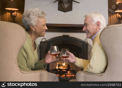 Couple sitting in living room by fireplace with drinks smiling