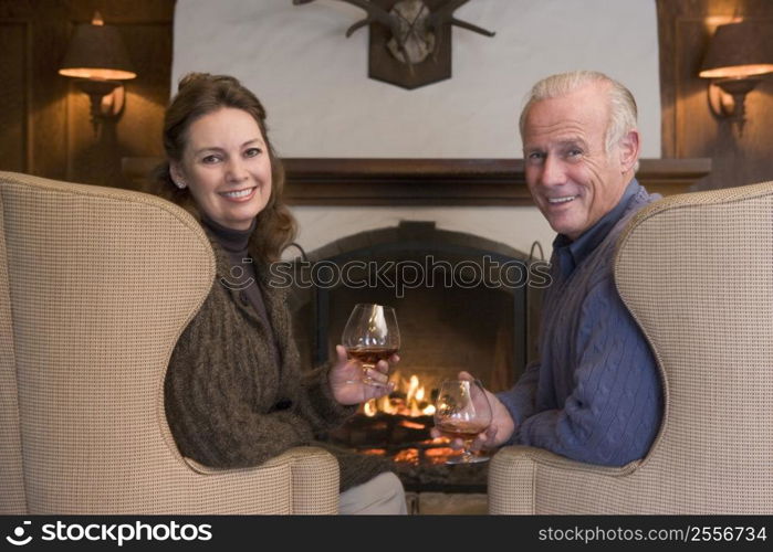 Couple sitting in living room by fireplace with drinks smiling