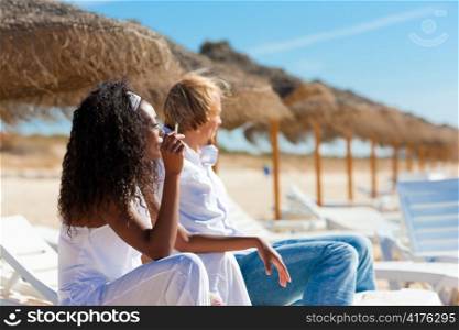 Couple sitting in sun chairs under on a beach enjoying the sun smoking a cigarette
