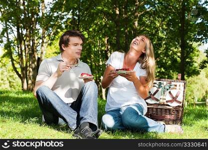 Couple sitting in the grass in summer having a picnic with strawberry cake