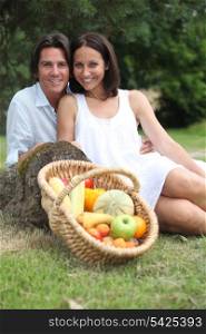 Couple sitting in the grass with fruit basket