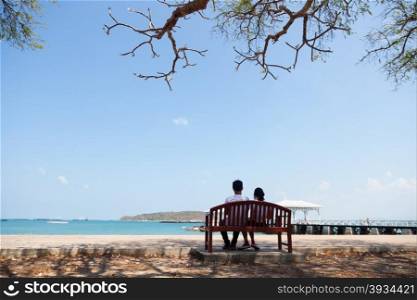 Couple sitting on a bench under a tree. The sea front Romantic couples