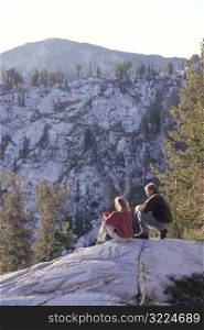 Couple Sitting On A Mountain Rock Watching The Sunrise