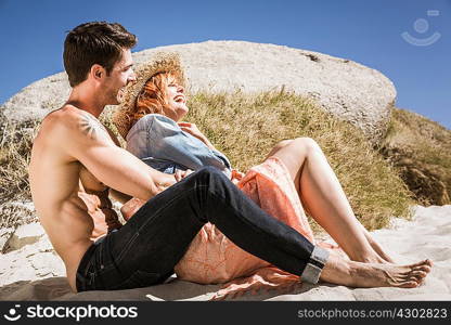 Couple sitting on beach, beside rocks, laughing
