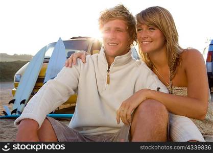 Couple sitting on beach smiling with van