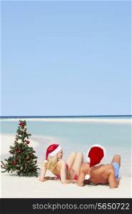 Couple Sitting On Beach With Christmas Tree And Hats