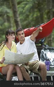 Couple sitting on car looking at map, man pointing