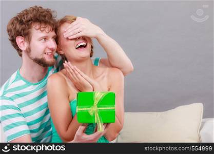 Couple sitting on couch at home. Young man giving woman gift box