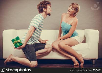 Couple sitting on couch at home. Young man giving woman gift box filtered photo