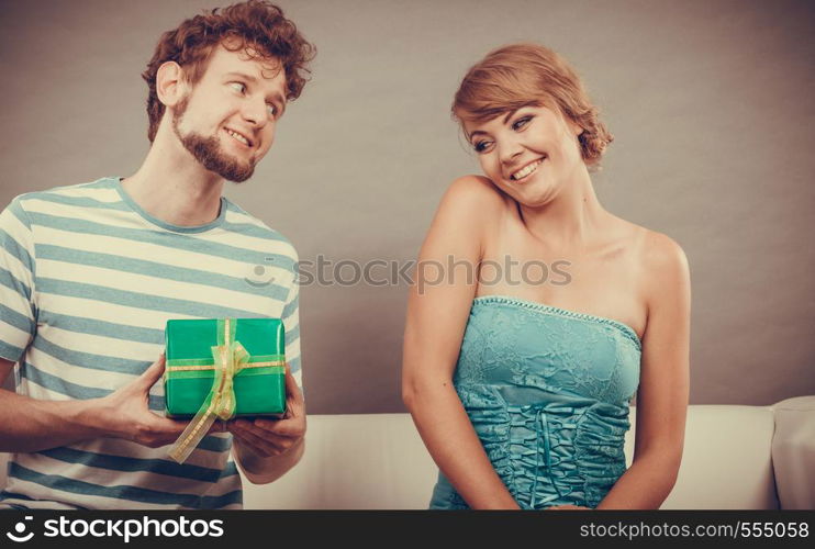 Couple sitting on couch at home. Young man giving woman gift box filtered photo