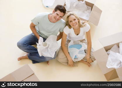 Couple sitting on floor by open boxes in new home smiling