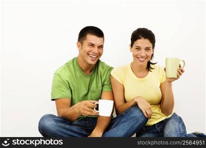 Couple sitting on floor drinking coffee and smiling.