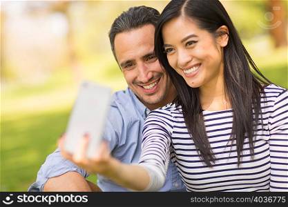 Couple sitting on grass using smartphone to take selfie