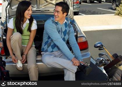 Couple Sitting on Rear Bumper of Car Putting on Golf Shoes