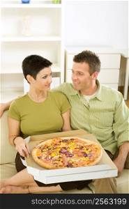 Couple sitting on sofa and eating pizza at home.