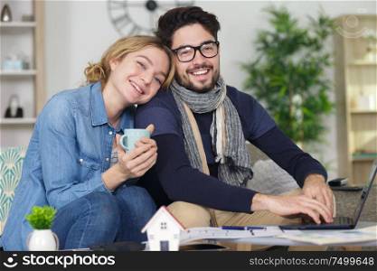 couple sitting on sofa drinking coffe or tea using laptop