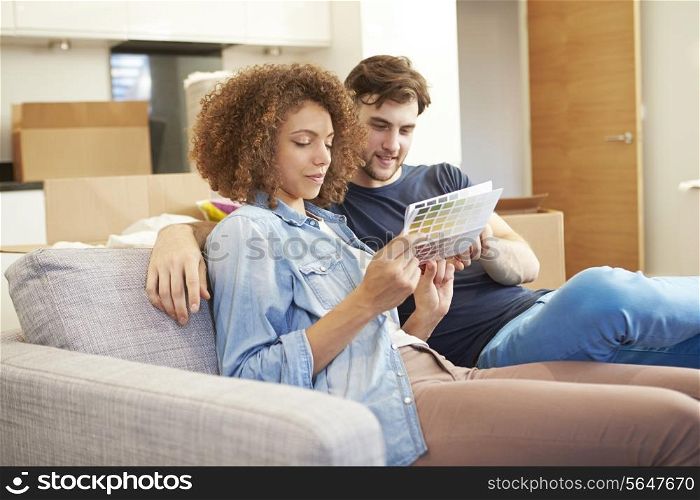 Couple Sitting On Sofa Looking At Paint Charts