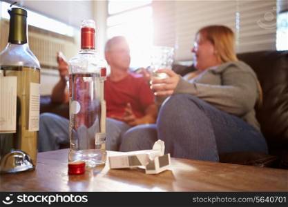Couple Sitting On Sofa With Bottle Of Vodka And Cigarettes