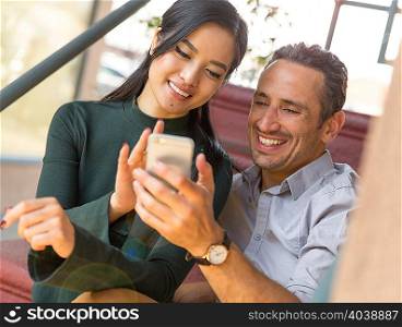 Couple sitting on stairway using smartphone smiling
