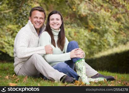Couple sitting outdoors embracing and smiling (selective focus)