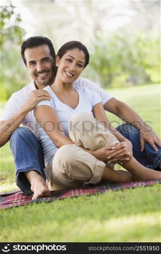 Couple sitting outdoors in park smiling (selective focus)
