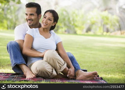 Couple sitting outdoors in park smiling (selective focus)