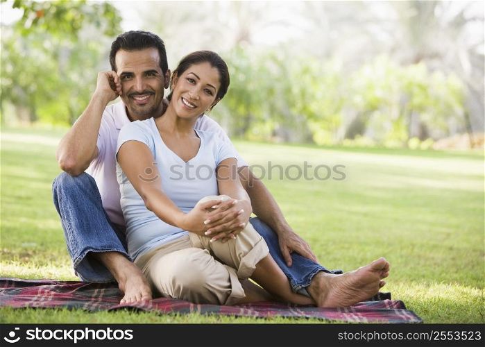 Couple sitting outdoors in park smiling (selective focus)