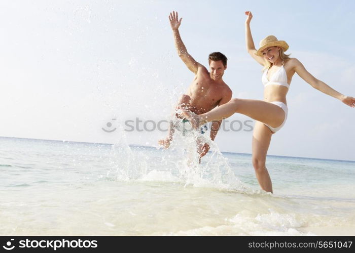 Couple Splashing In Sea On Beach Holiday