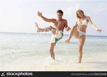 Couple Splashing In Sea On Beach Holiday
