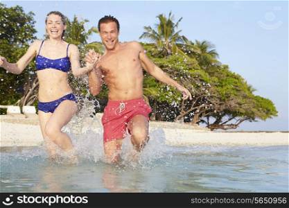 Couple Splashing In Sea On Tropical Beach Holiday