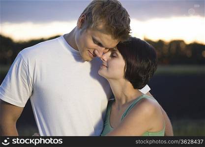 Couple stand embracing with eyes closed in evening light