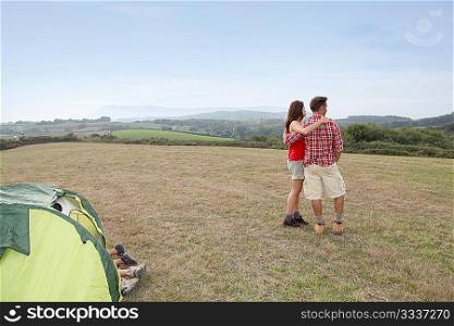 Couple standind by camp tent and looking at scenery