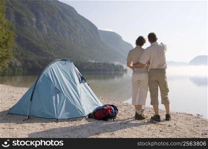 Couple standing beside a tent at a mountain lake on a misty morning