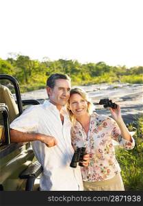 Couple standing by jeep holding binoculars smiling