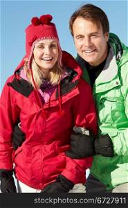 Couple Standing In Snow Wearing Warm Clothes On Ski Holiday In Mountains