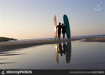 Couple standing on beach with surfboards