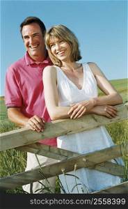 Couple standing outdoors by fence smiling