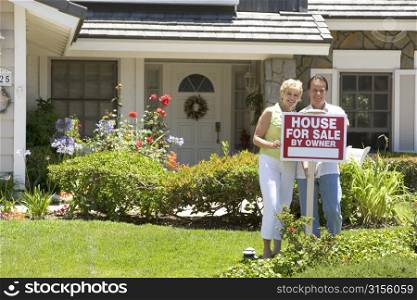 Couple Standing Outside House With Real Estate Sign