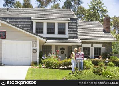 Couple Standing Outside House With Real Estate Sign