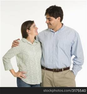 Couple standing smiling at eachother against white background.