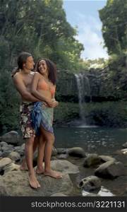 Couple Standing Together On Rock In Front Of Tropical Waterfall