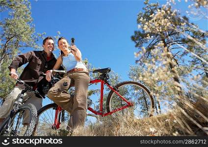 Couple standing with mountain bikes using mobile phone photographing selves low angle view.