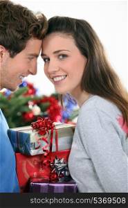 Couple stood by Christmas tree and gifts