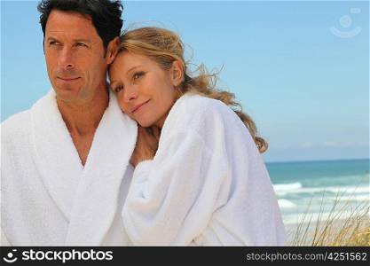 Couple stood on beach wearing bath gowns