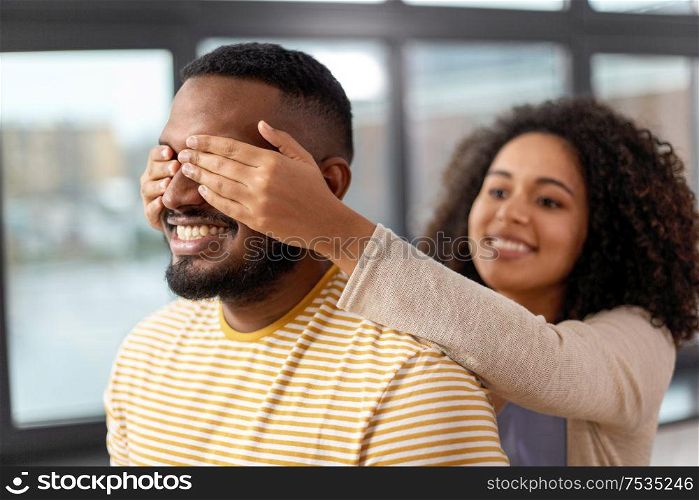 couple, surprise and relationships concept - happy african american woman closing man&rsquo;s eyes at home. happy african american woman closing man&rsquo;s eyes